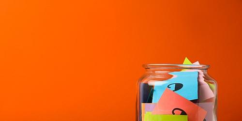 glass jar filled with colourful pieces of paper with question marks